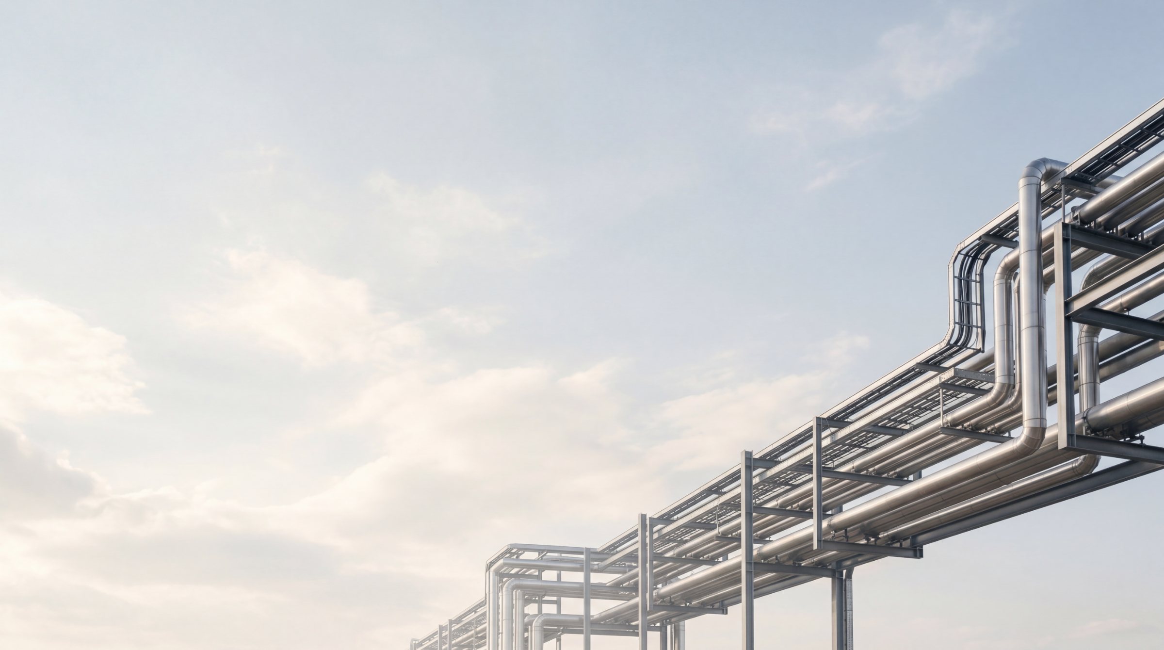 Industrial pipe rack silhouetted against a soft daytime sky