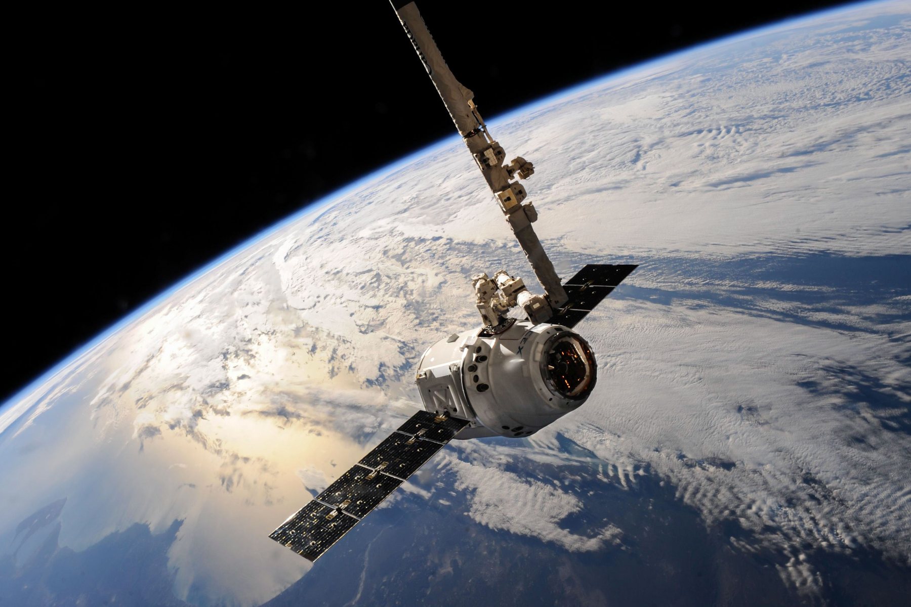 Cargo spacecraft berthed by robotic arm above Earth